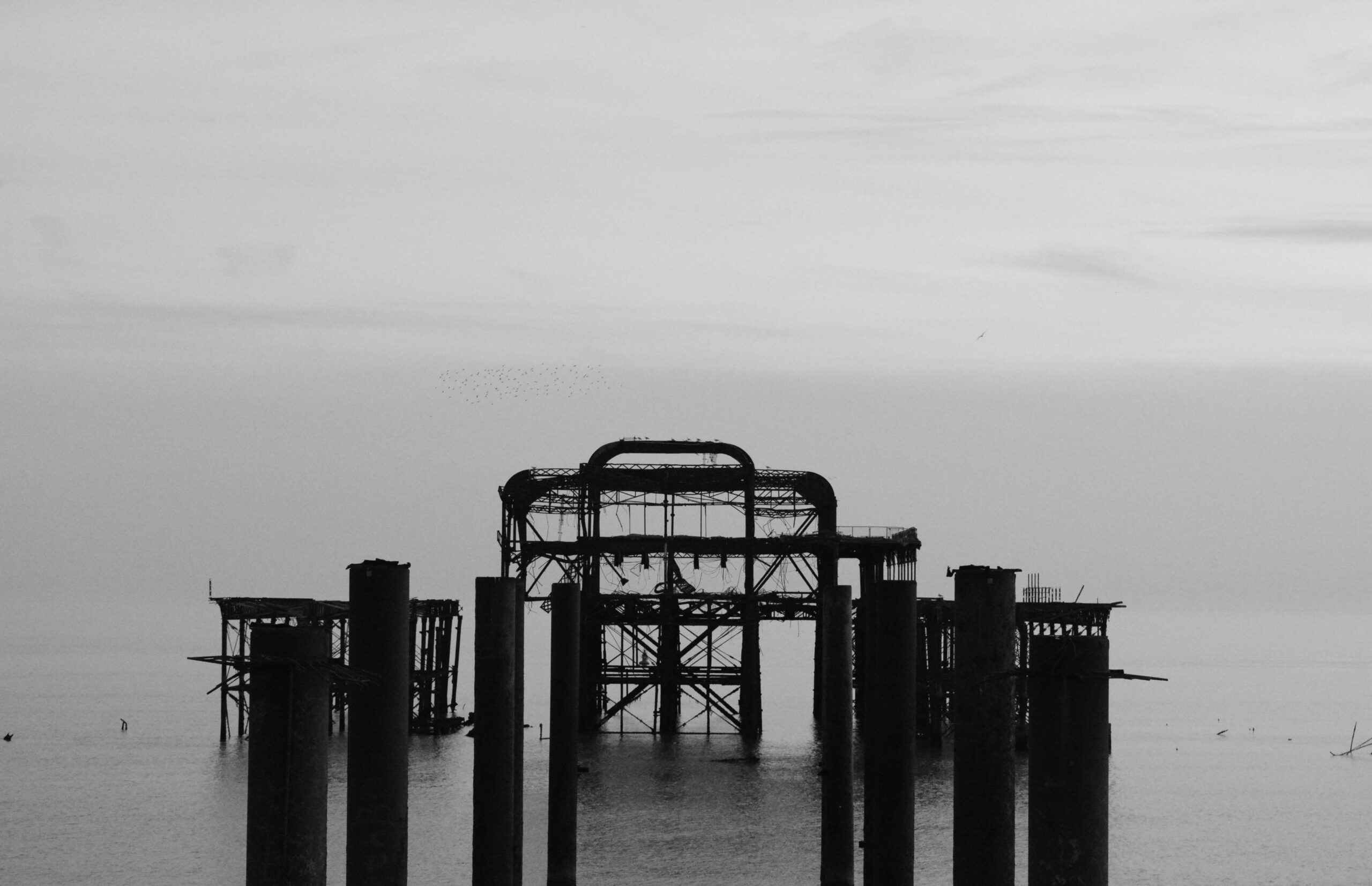 The West Pier ruins in black and white under a still grey sky