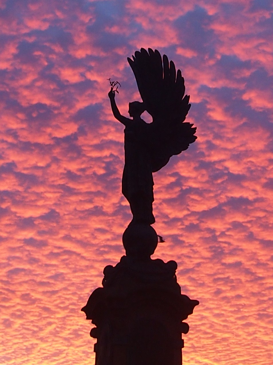 The Peace Statue silhouetted against a pink and orange sky